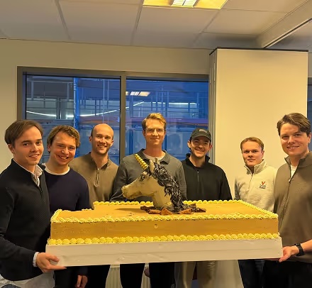 A team standing behind a long cake topped with a unicorn head